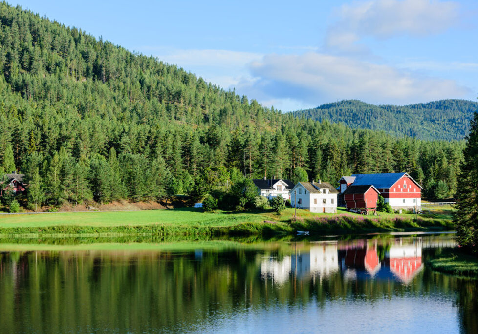 Small village with two main houses and some farm buildings situated in forest landscape at a tranquil river bend. Location Skutsvika along route 40 in Norway.